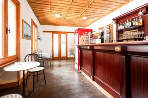 Una zona de bar con techo de madera, una barra con botellas y un área de estar con mesas y sillas.