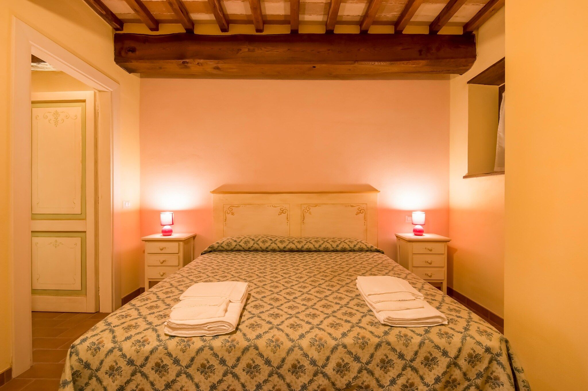 Quarto com cama, duas mesas de cabeceira e uma porta.