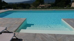 Ein rechteckiger Pool mit klarem, blauem Wasser, umgeben von Steinplatten. Liegestühle befinden sich im Vordergrund.