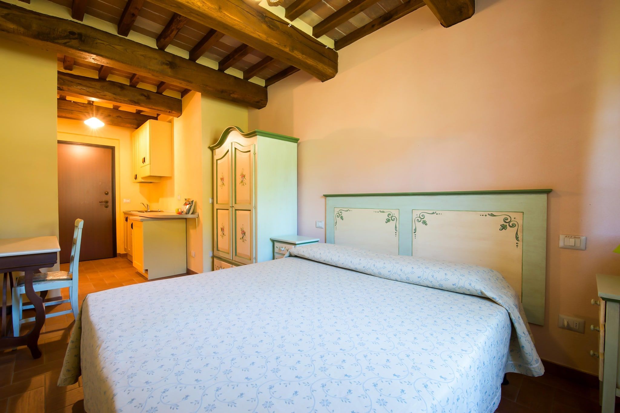 Quarto com cama, teto de madeira, guarda-roupa e uma pequena cozinha.