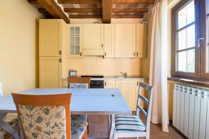 A kitchen with wooden cabinets, a dining table, chairs, and a window with curtains. - Beautiful farmhouse with swimming pool (Città di Castello)