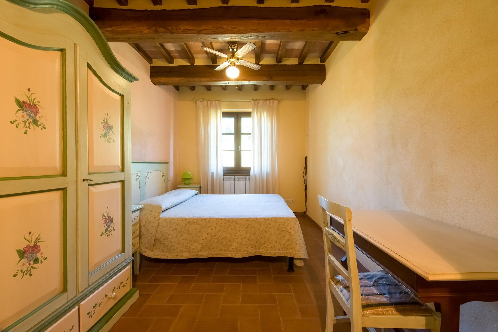 A bedroom with a bed, a chair, a window with curtains, and a radiator.