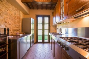 A kitchen with a stone wall, a refrigerator, a stove, and a door leading outside. - Beautiful farmhouse with swimming pool (Città di Castello)