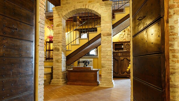 Ein mit Steinmauern ausgekleideter Gang mit einer hölzernen Truhe, einer Treppe und einer großen Holztür.