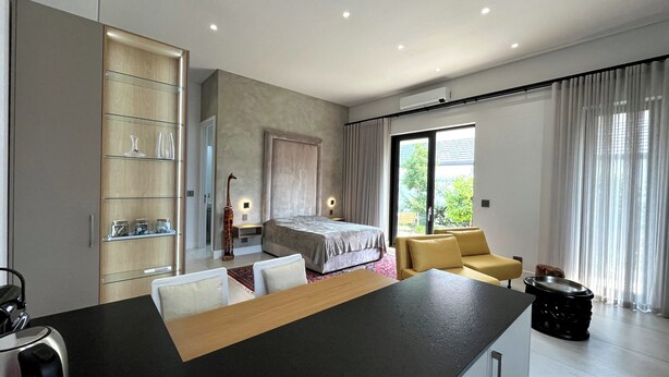A modern bedroom with a bed, a sofa, a dining table, and a kitchen area.