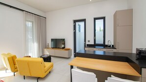 A modern living room with a sofa, a dining table, and a kitchen area with a TV and cabinets.