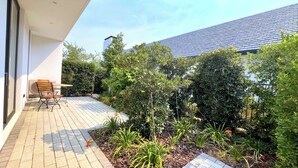 A patio with a table and chairs, surrounded by well-maintained shrubs and plants.