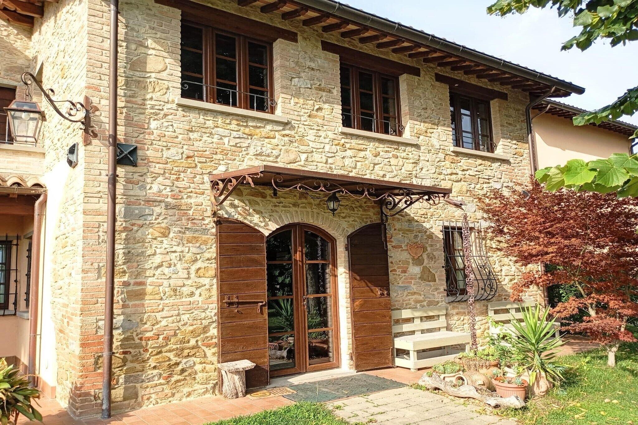 Un edificio in pietra con un portico in legno, ampie finestre e un giardino curato.