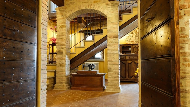 A stone-walled hallway with a wooden chest, a staircase, and a large wooden door.