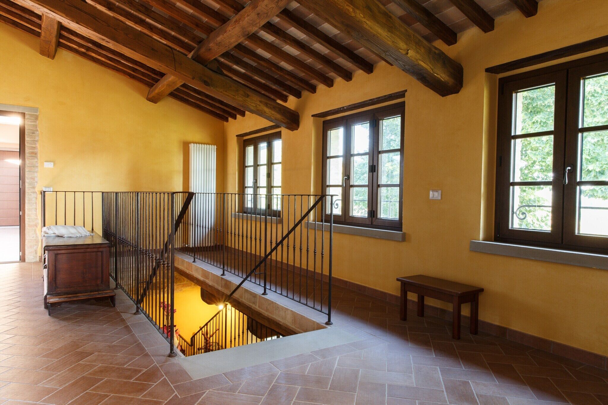 A spacious interior with a tiled floor, a wooden staircase with a metal railing, and large windows allowing natural light.