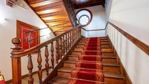 A wooden staircase with a red carpet, a wooden handrail, and a round window at the top.