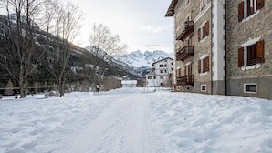 A snow-covered path leading to a building with balconies and a mountainous backdrop.