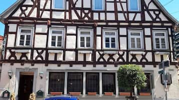 A traditional half-timbered building with multiple windows, a car parked in front, and a small tree in the foreground.