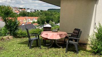Eine Terrasse im Freien mit Tisch und Stühlen, umgeben von Grünpflanzen und mit Blick auf eine Wohngegend.