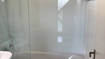 A bathroom with a glass-enclosed shower, a white bathtub, and a sink.