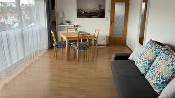 Ein Wohnzimmer mit Esstisch aus Holz, Stühlen, einer Couch, einer Topfpflanze und einem Stadtbild an der Wand.