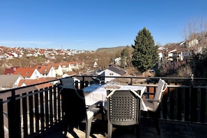 Un balcon avec une table et des chaises, donnant sur un quartier résidentiel avec des maisons et une colline au loin.