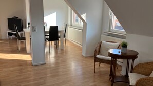 Un vaste espace de vie comprenant une table à manger, des chaises, un téléviseur et une vue sur l’extérieur.