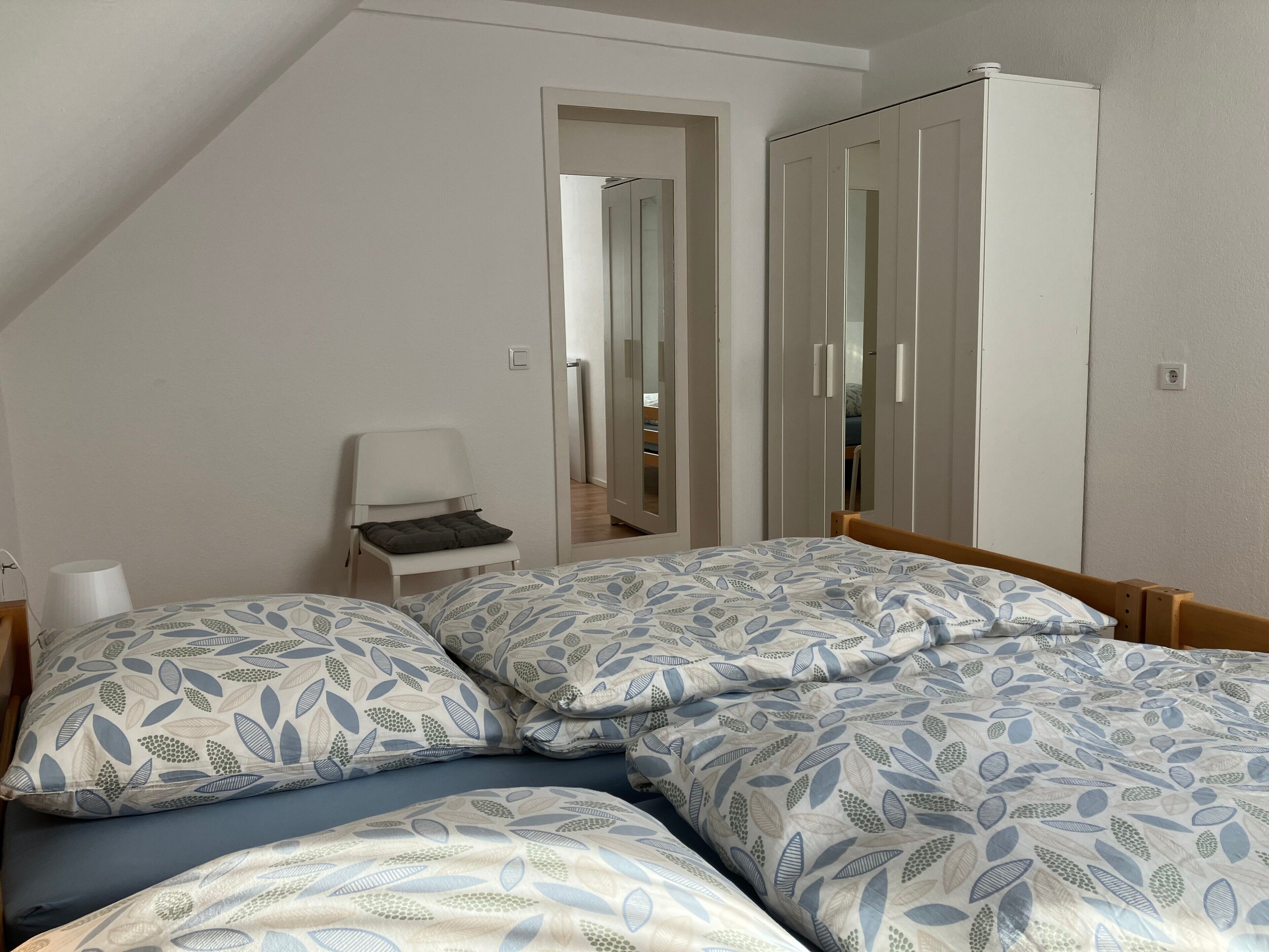 A bedroom with two beds, a chair, a wardrobe, and a mirror.