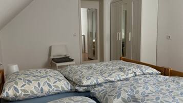 A bedroom with two beds, a chair, a wardrobe, and a mirror.