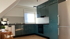 Une cuisine moderne avec des armoires de couleur turquoise, un réfrigérateur en acier inoxydable et un coin repas doté de meubles en osier.