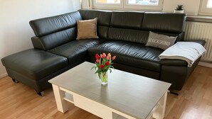 Un salon moderne avec un canapé en cuir noir, une table basse blanche et un vase de tulipes.
