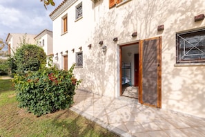 A two-story building with a tiled patio, a wooden door, and a small garden with red flowers. - Cozy Apartment 300mt From the Beach (Budoni)