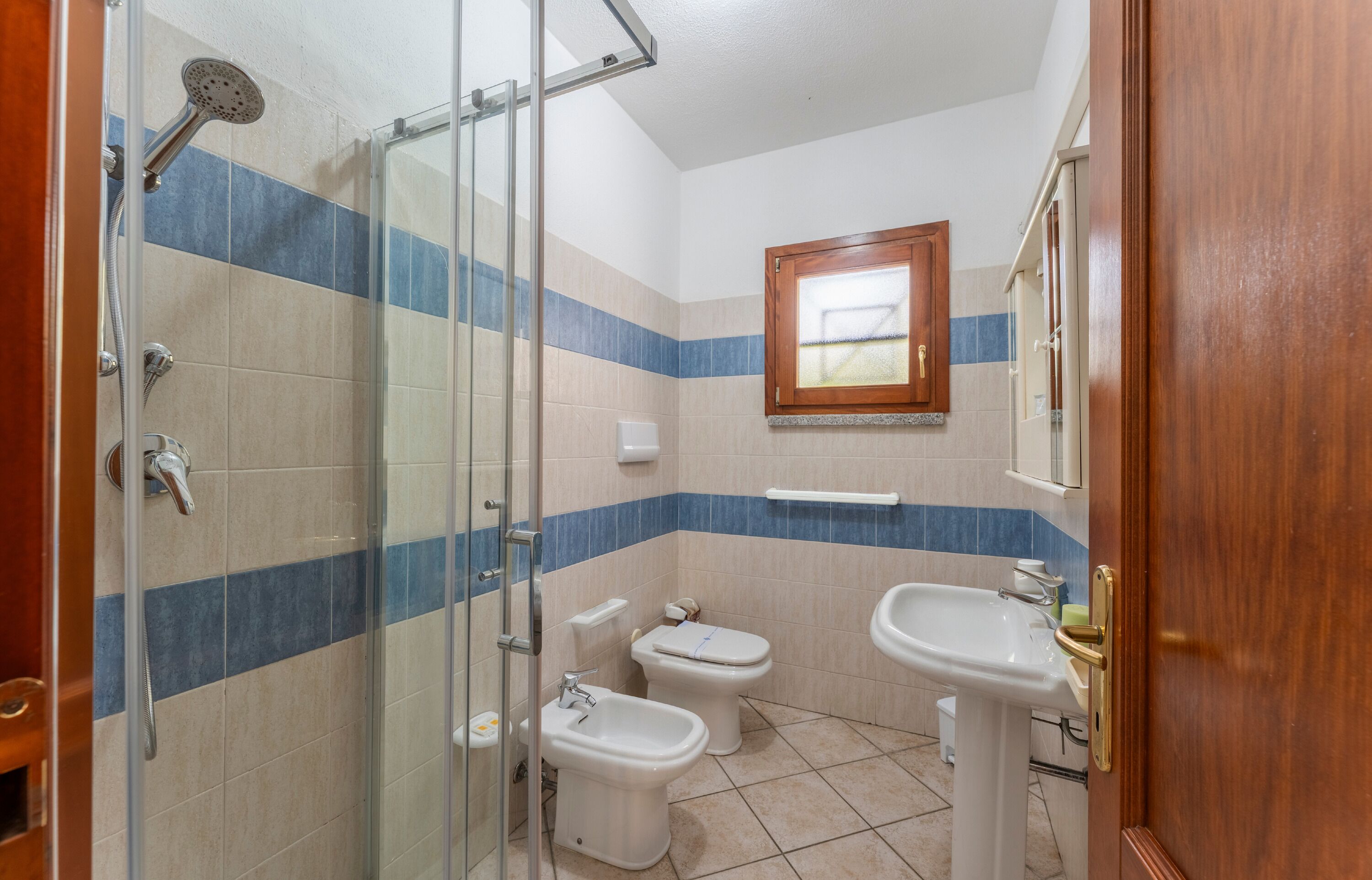 Un baño con cabina de ducha de vidrio, dos inodoros, un bidé y un lavabo.