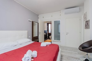 A hotel room with a red bedspread, white pillows, a black chair, and a bathroom visible through an open door.