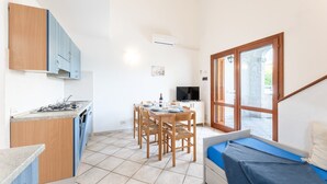 A compact kitchen with a dining area, a TV, and a window with blinds. - Spacious Flat 300mt From the Beach (Budoni)