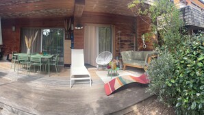 En træterrasse med et spisebord og stole, en hvid liggestol og en sofa.