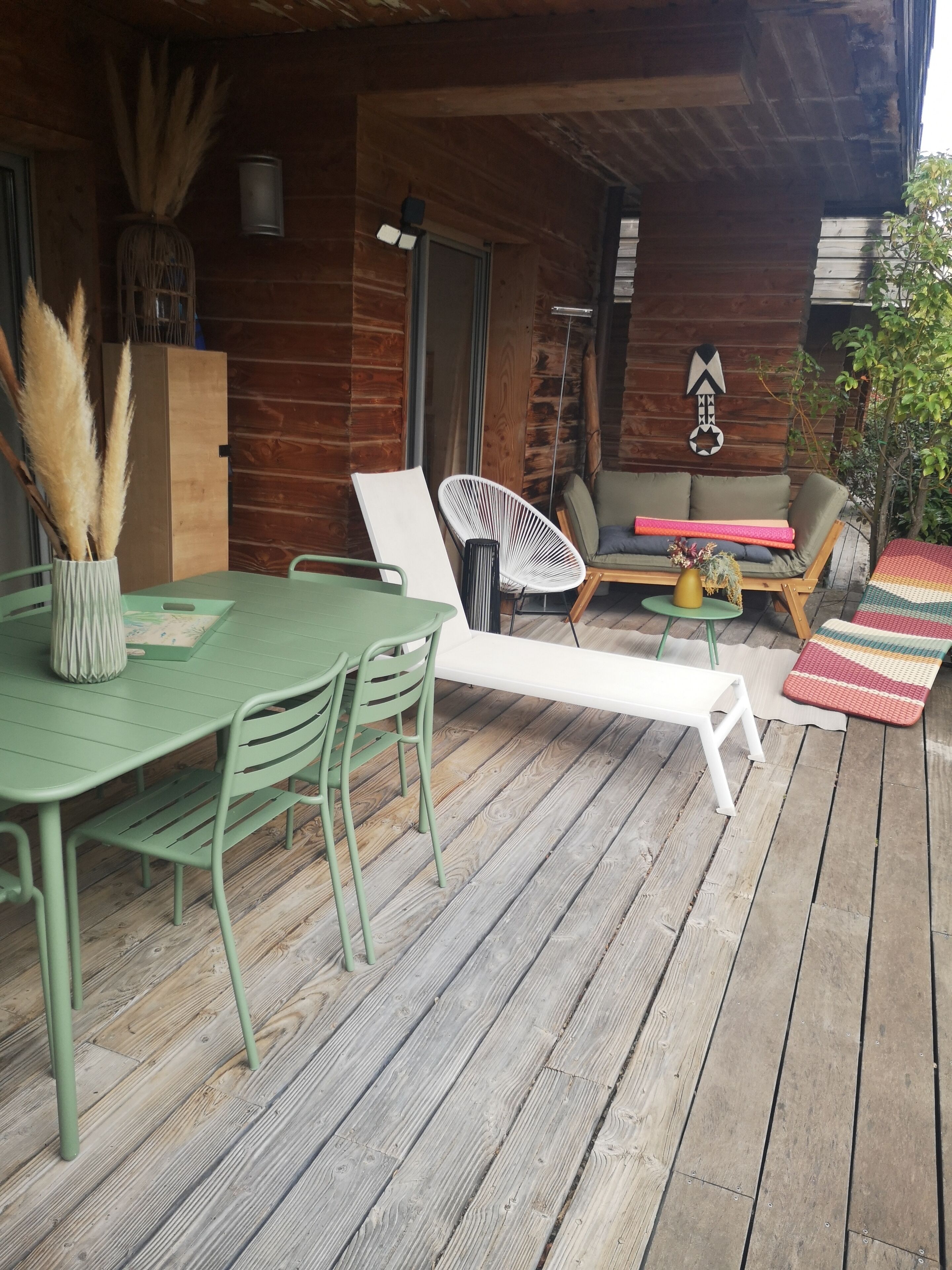 Een houten terras met een tafel, stoelen, een bank en een hangstoel.