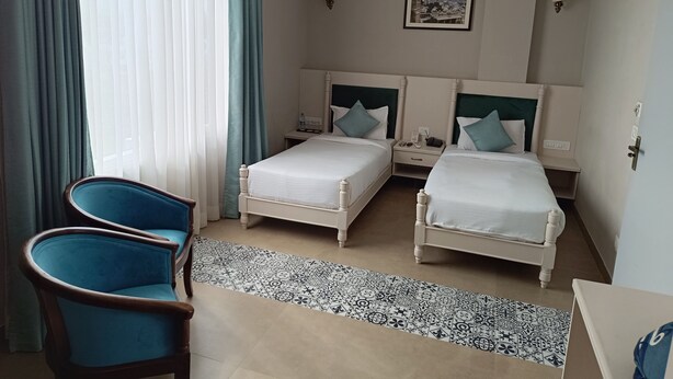 Une chambre d’hôtel avec deux lits, une chaise, une table de chevet, une lampe et un ventilateur de plafond.