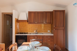 A compact kitchen with wooden cabinets, a gas stove, and a tiled backsplash. - Cozy Apartment Surrounded by Nature (Budoni)