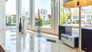 Ein modernes Wohnzimmer mit großem Fenster, einer dekorativen Stehlampe, einer Fernbedienung und einer Philips-Audiosystem.
