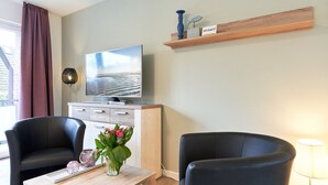 Een moderne woonkamer met een flatscreen televisie, twee zwarte stoelen, een houten salontafel en een vaas met bloemen.