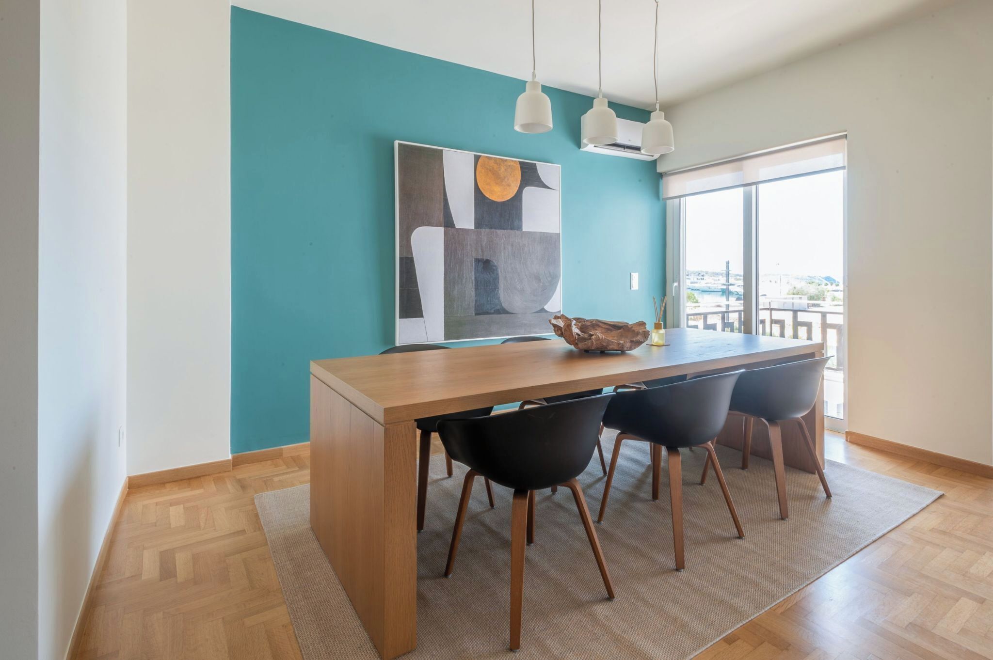 A dining area with a wooden table, black chairs, a teal accent wall, and a large abstract painting.