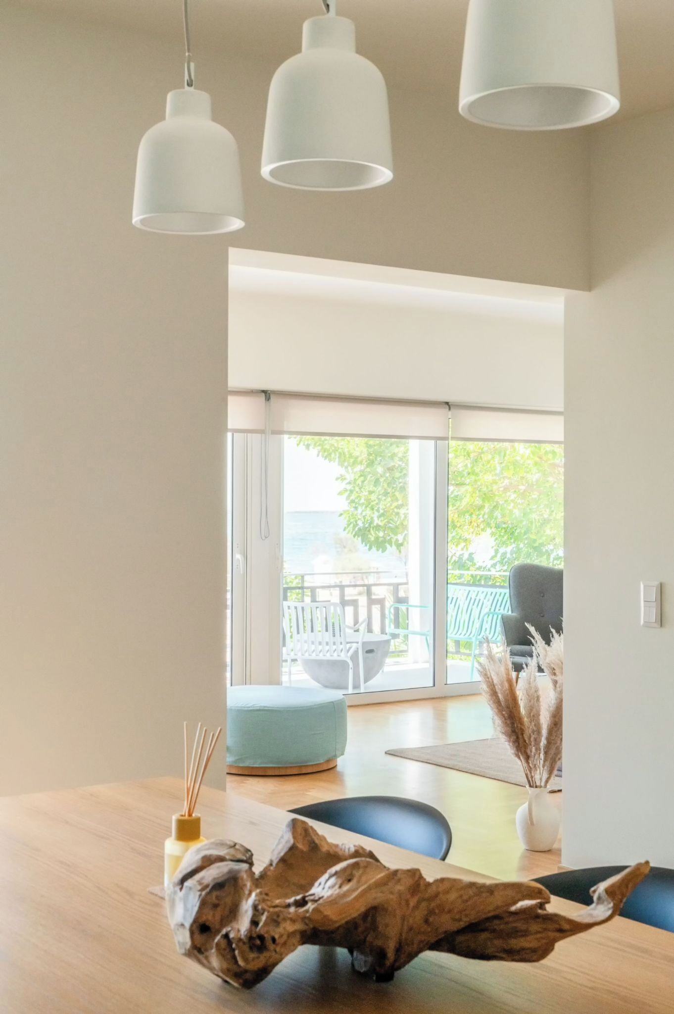 Un interior moderno con una mesa de comedor de madera, una silla azul y vistas a un patio exterior con una mesa y sillas.