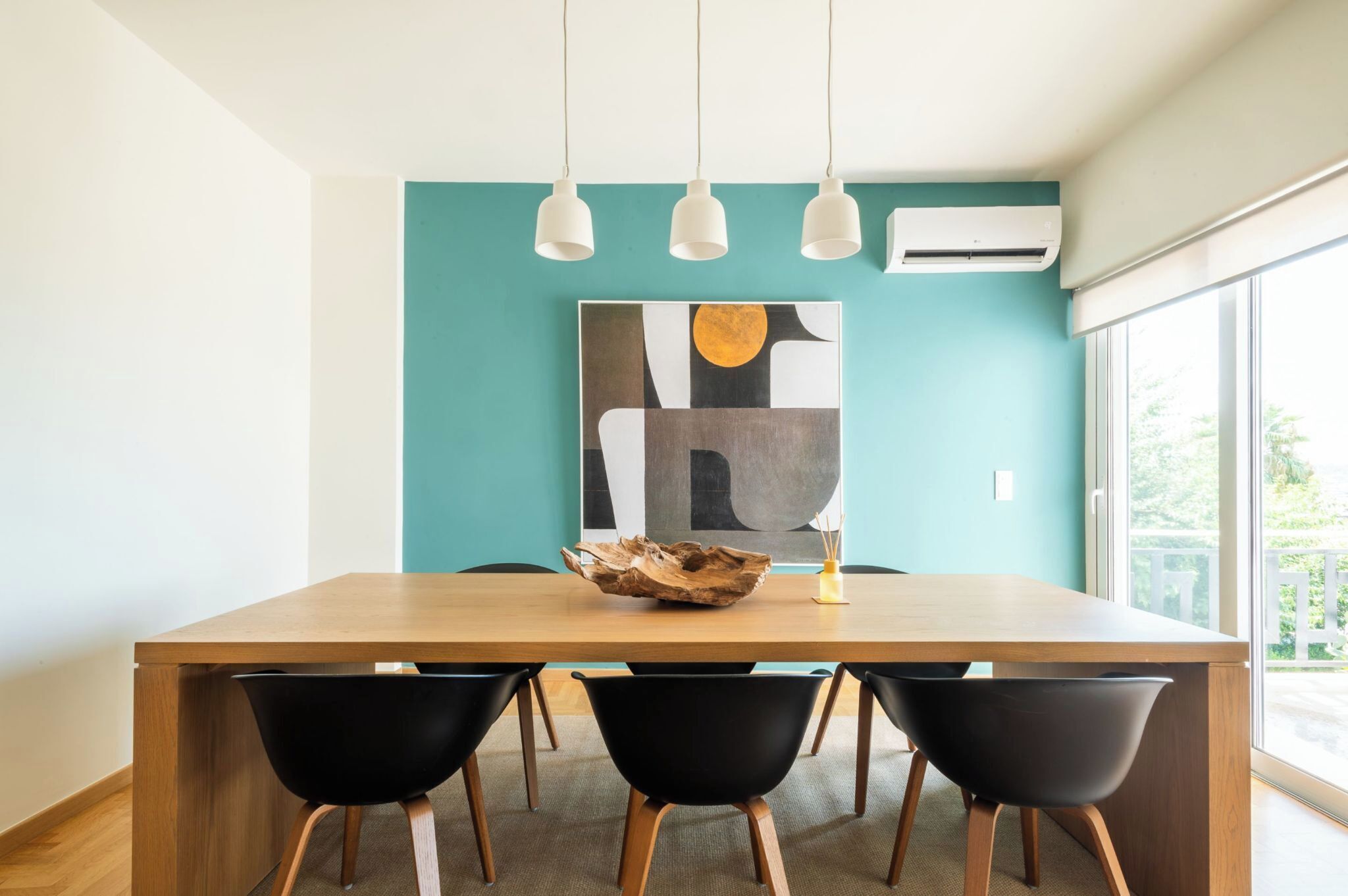Un comedor moderno con una mesa de madera, sillas negras y un cuadro abstracto grande en una pared verde azulado.