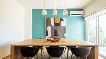 Un comedor moderno con una mesa de madera, sillas negras y un cuadro abstracto grande en una pared verde azulado.