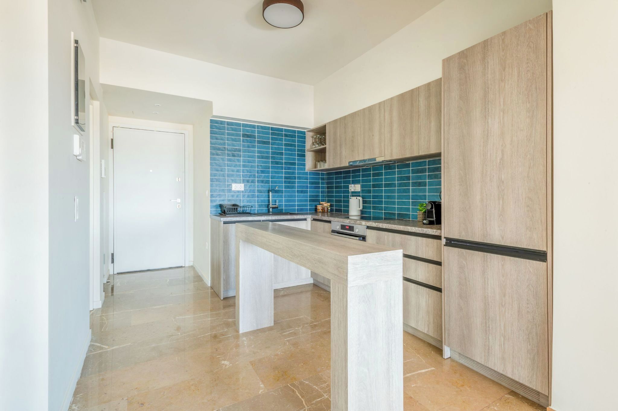 Una cocina moderna con una isla central, salpicadero azul y armarios de madera clara.