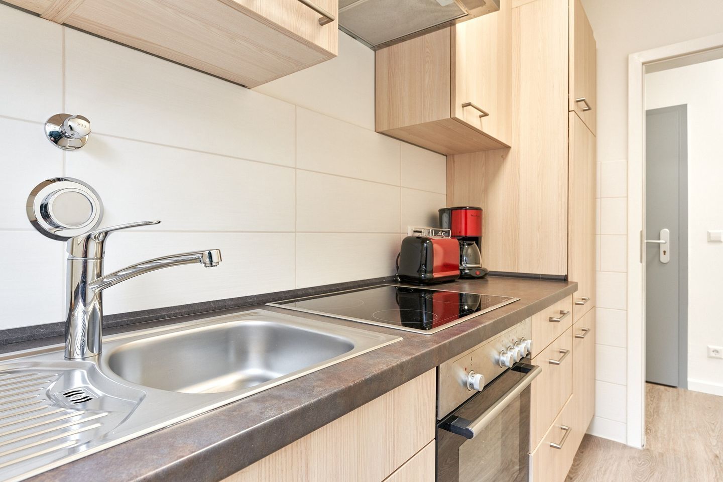 Una cocina moderna con un lavamanos doble, grifo de acero inoxidable, placa de inducción negra y una cafetera roja.