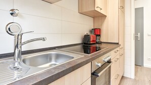 Une cuisine moderne dotée d’un évier à deux bacs, d’un robinet en acier inoxydable, d’une plaque de cuisson à induction noire et d’une machine à café rouge.