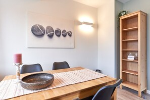 A dining area with a wooden table, chairs, a decorative bowl, a pink candle, and a wall-mounted light fixture. - Haus SeeZeit, Apartment 07 - Haus SeeZeit (Timmendorfer Strand)