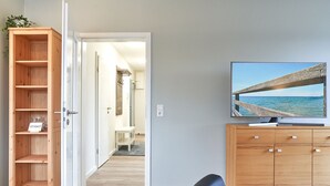 Een moderne woonkamer met een houten kast, een flatscreen televisie aan de muur en uitzicht op zee door een raam.