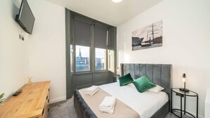 A bedroom with a bed, a desk, a TV, a window, and a painting on the wall. - Dockside: Quay Views, City Vibes (Dundee)