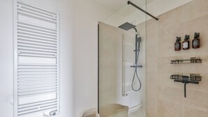 Une salle de bain moderne avec une douche à parois de verre, un radiateur blanc et des produits de toilette fixés au mur.