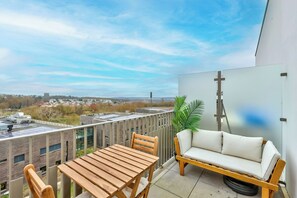 A balcony with a wooden table and chairs, a white sofa, and a potted plant. - Beautiful 1-bedroom apartment with a lovely terrace and parking space (Torcy)