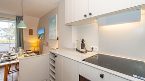 A modern kitchen with white cabinetry, a built-in stove, and a large window providing natural light. - Syltweh - Comfortable Syltweh vacation apartment with south-facing balcony in Munkmarsch (Sylt)
