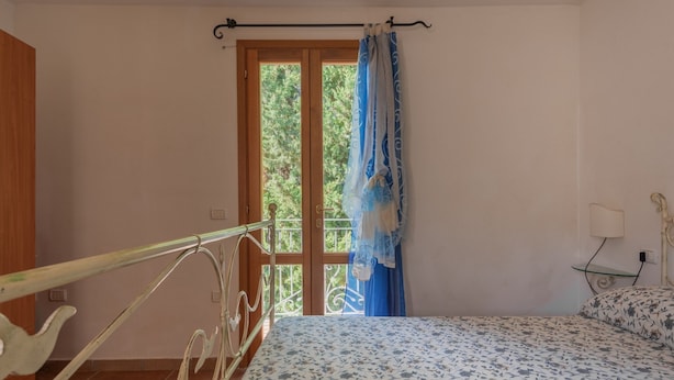Ein Schlafzimmer mit Bett, einem Fenster mit Vorhängen, einem Metallbettgestell und einem kleinen Nachttisch.
